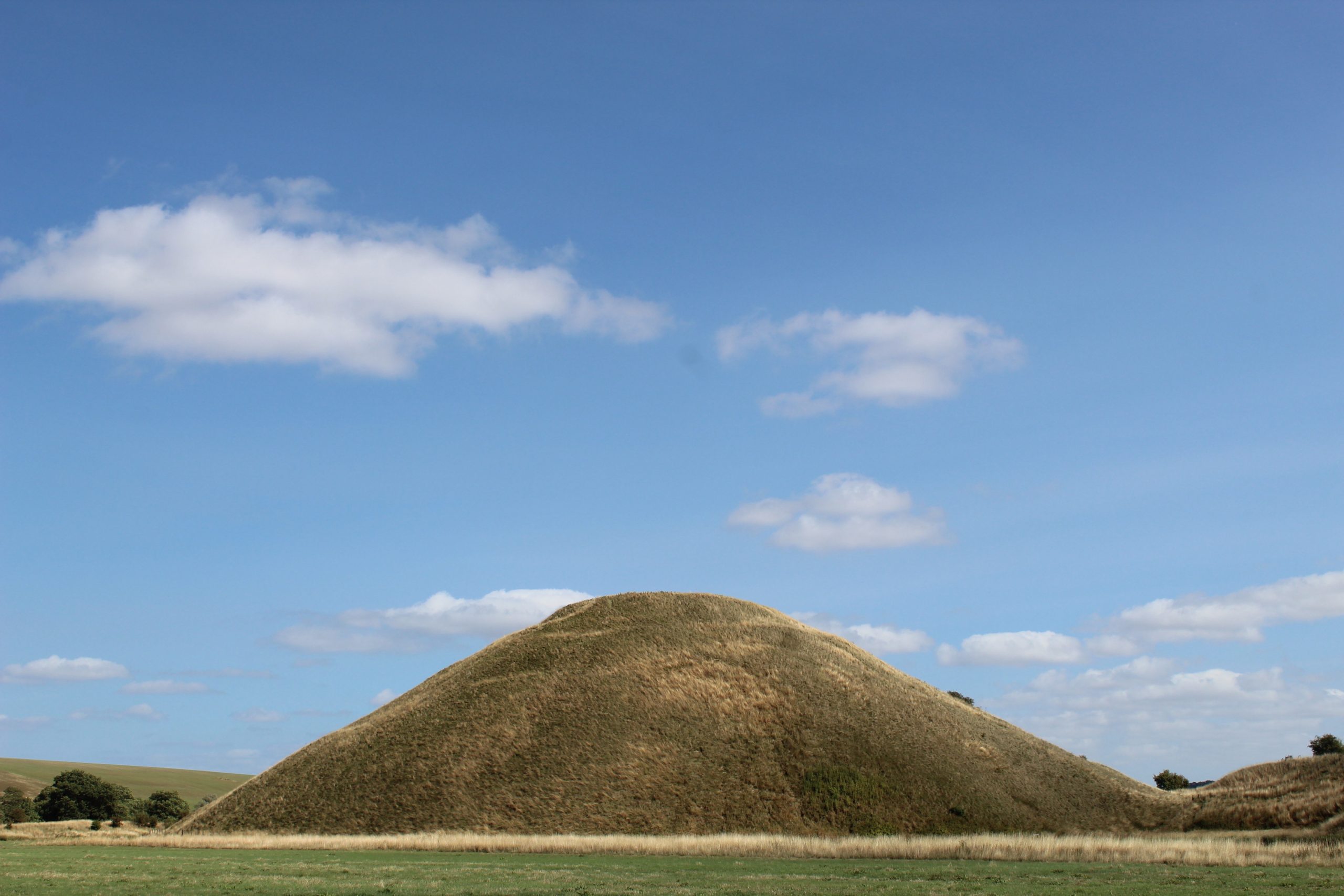 Silbury Hill, the largest prehistoric artificial mound in Europe, covered in grass and surrounded by the Wiltshire countryside on a clear day.